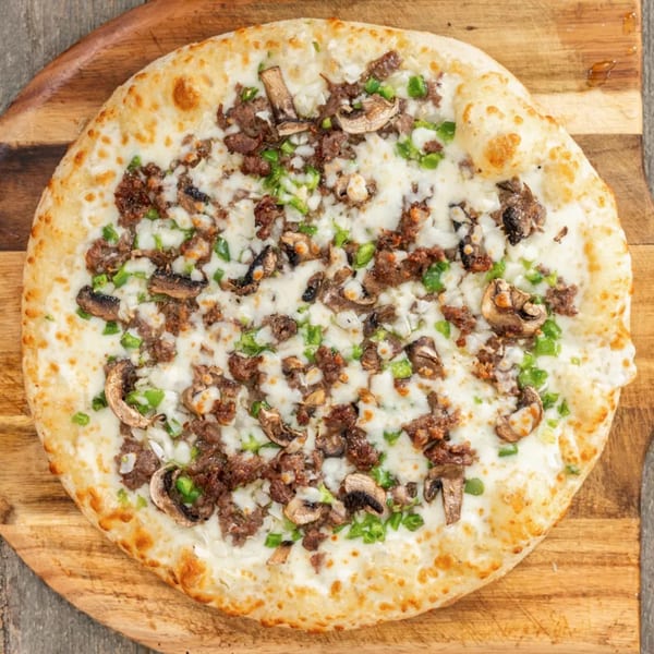 A whole pizza with white cheese, ground meat, mushrooms, and green peppers on a wooden board.