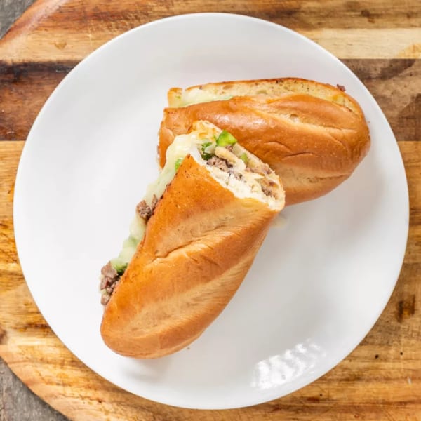 Two halves of a cheesesteak sandwich with meat, cheese, and green peppers on a white plate.