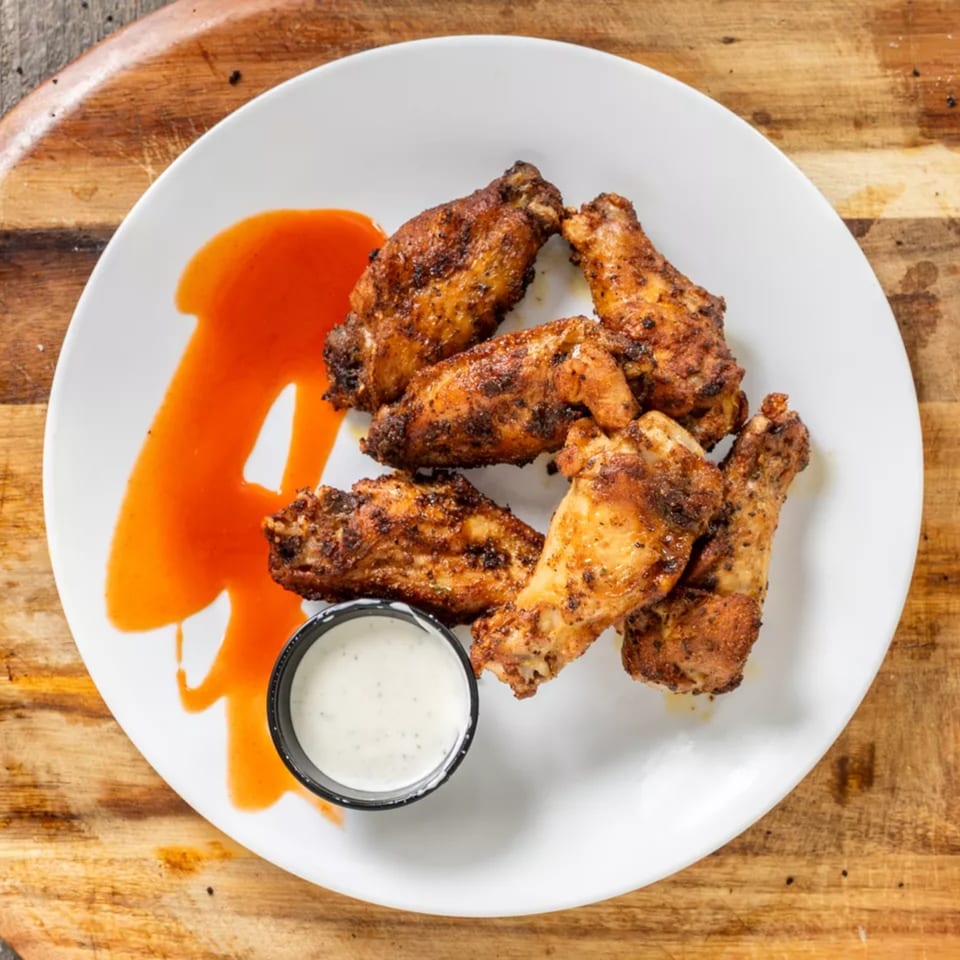 Crispy chicken wings with hot sauce and ranch dressing on a white plate.