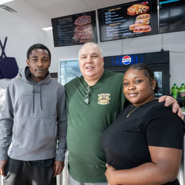 Three smiling restaurant staff members, two men and one woman, stand together in a casual setting.
