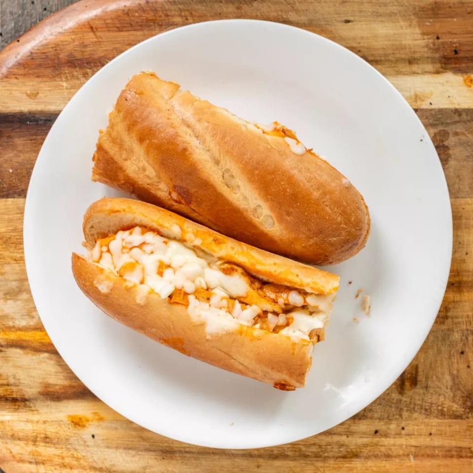 Two golden-brown bread rolls filled with melted white cheese and a reddish sauce on a white plate.