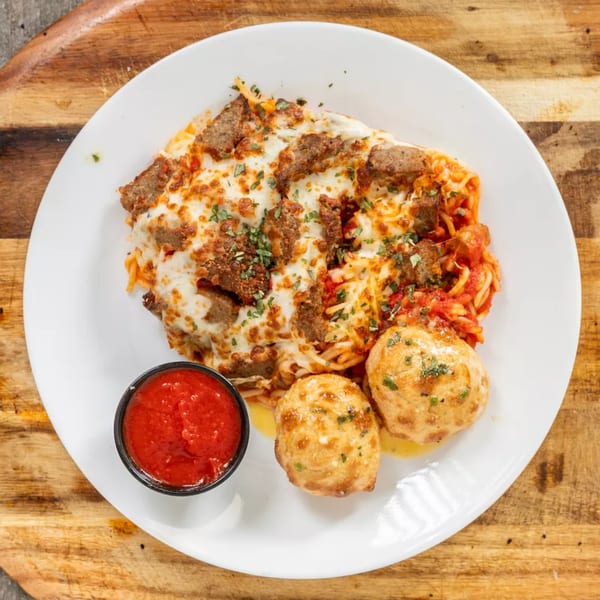 Baked spaghetti with melted cheese, sausage, and two bread rolls with a side of marinara sauce.