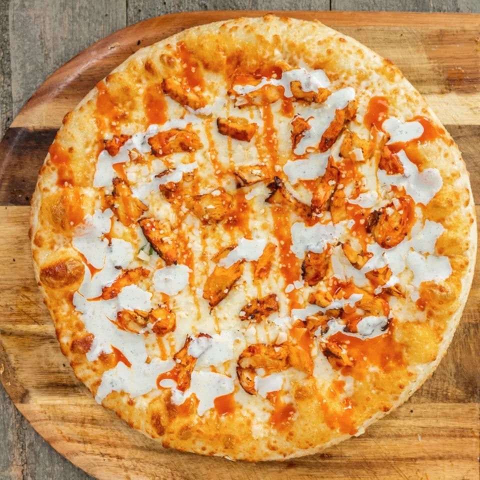 Buffalo chicken pizza with ranch and hot sauce drizzle on a wooden serving board.